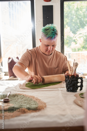 Man with special needs holding rolling pin and rolls out green leaf at the clay
