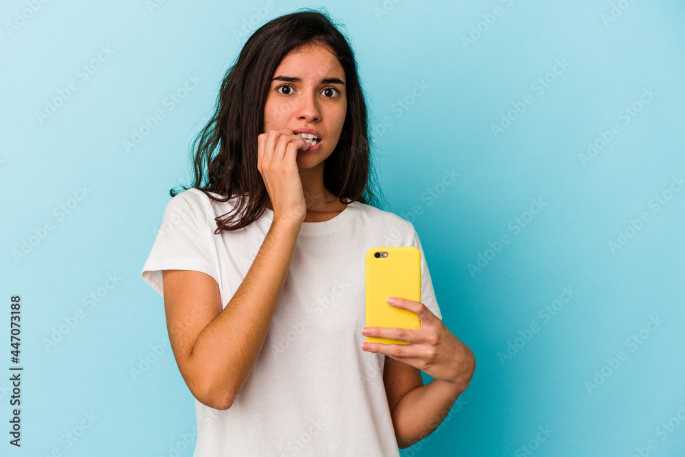 Young caucasian woman holding a mobile phone isolated on blue background biting fingernails, nervous and very anxious. Young caucasian woman holding a mobile phone isolated on blue background biting fingernails, nervous and very anxious.