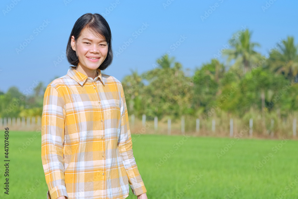 An Asian woman wearing a yellow striped shirt is standing smiling in a field. An Asian woman wearing a yellow striped shirt is standing smiling in a field.