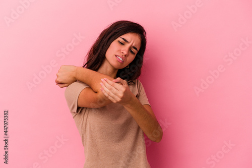 Young caucasian woman isolated on pink background massaging elbow, suffering after a bad movement.