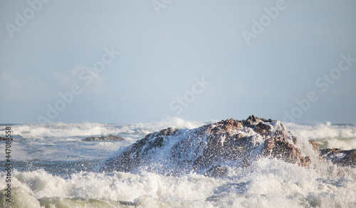 Crashing waves on rocks at sunset on shoreline.