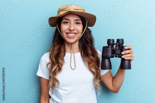 Young mexican woman holding binoculars isolated on blue background happy, smiling and cheerful. © Asier