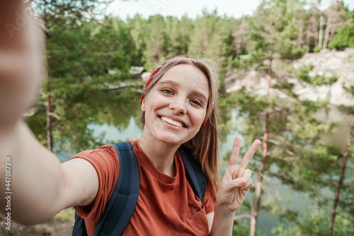 The young happy tourist left the city for the weekend, records video vlogs from her trip on her phone, sends greetings to her friends on social networks showing a peace sign with her hand