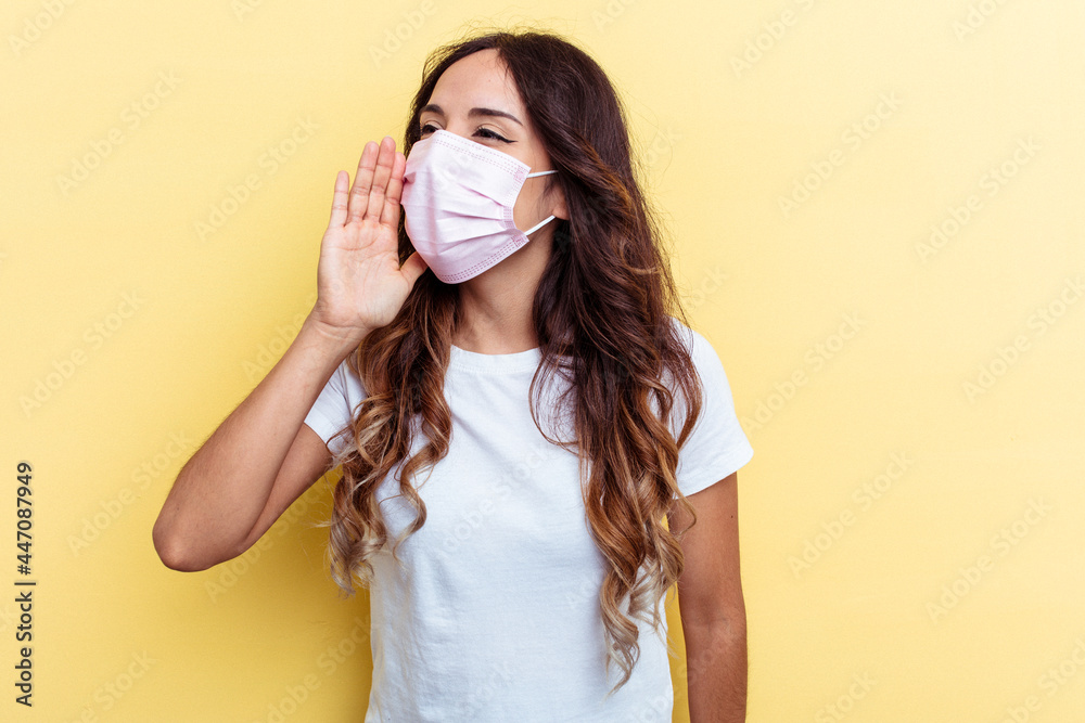 Young mixed race woman wearing a protection for virus isolated on yellow background shouting and holding palm near opened mouth. Young mixed race woman wearing a protection for virus isolated on yellow background shouting and holding palm near opened mouth.