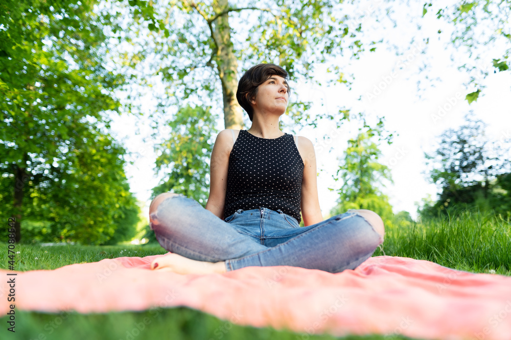 Portrait of an attractive young female sitting with her legs crossed in the park and enjoying summertime in Hyde Park, London