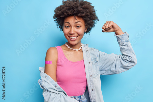 Papier peint Photo of satisfied curly haired woman raises arm shows biceps wears pink t shirt