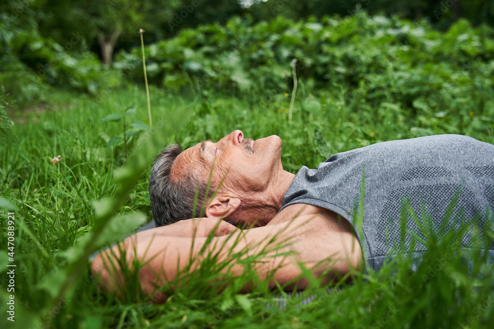 Man laying at the yoga mat at the grass after exercises and relaxing