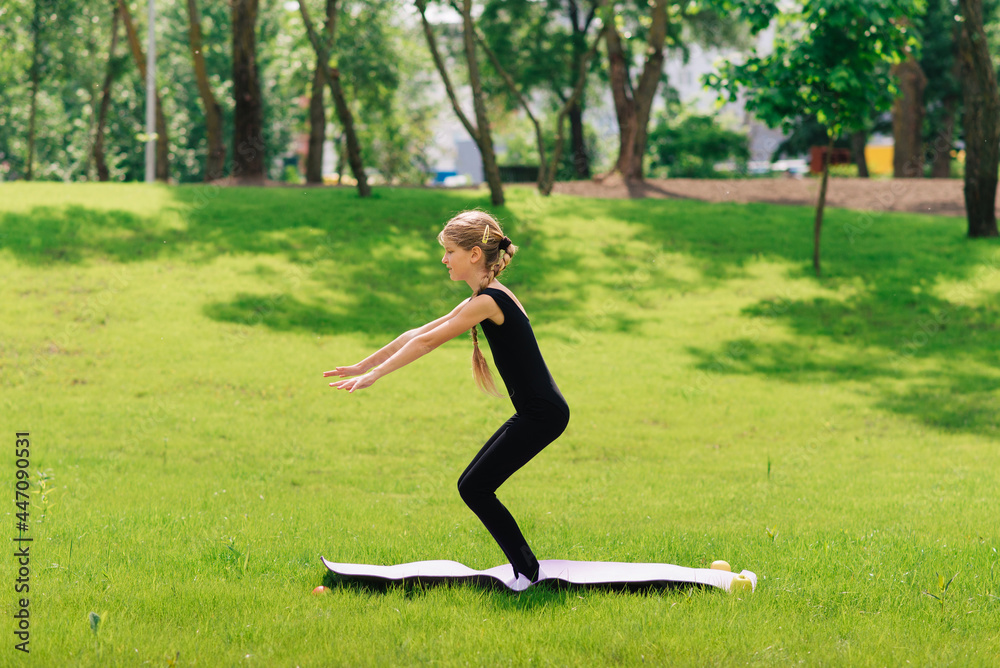slim girl in a black gymnastic uniform performs gymnastic exercises or pilates on the green grass in the park. Professional gymnast during training slim girl in a black gymnastic uniform performs gymnastic exercises or pilates on the green grass in the park. Professional gymnast during training
