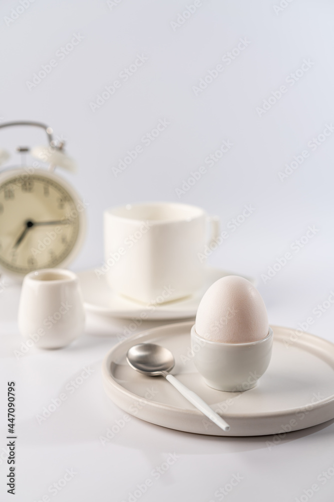 White egg with white plates, cup and alarm clock over white background for breakfast White egg with white plates, cup and alarm clock over white background for breakfast