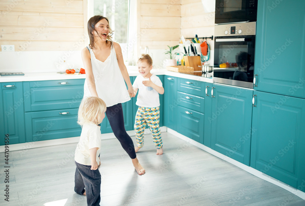 Small children brothers and mother play fun games in the kitchen in the house. Good mood in the morning. Comfortable home clothes for children. Small children brothers and mother play fun games in the kitchen in the house. Good mood in the morning. Comfortable home clothes for children.