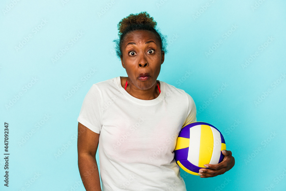 Young african american woman playing volleyball isolated on blue background shrugs shoulders and open eyes confused.