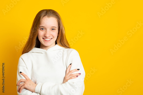 Beautiful teenage girl in a white hoodie cute smiling on yellow background.
