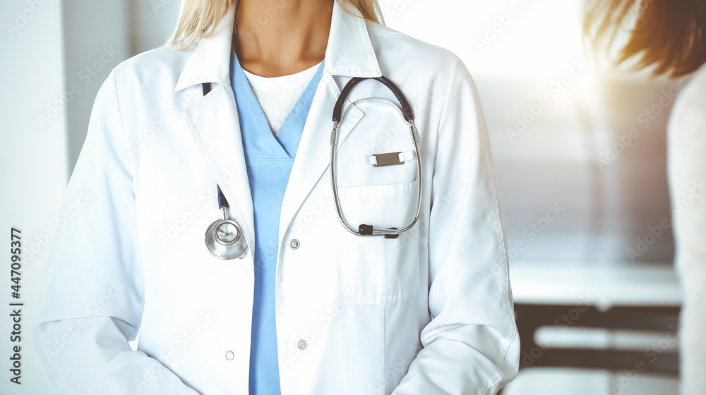 Unknown woman-doctor and patient in sunny hospital. Physician controls medication history records and exam results while using clipboard, close-up Unknown woman-doctor and patient in sunny hospital. Physician controls medication history records and exam results while using clipboard, close-up