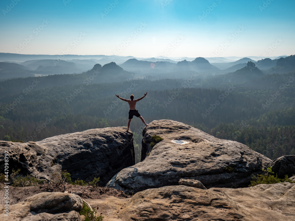 Shirtless male silhouette with raised arms on sharp mountain top.