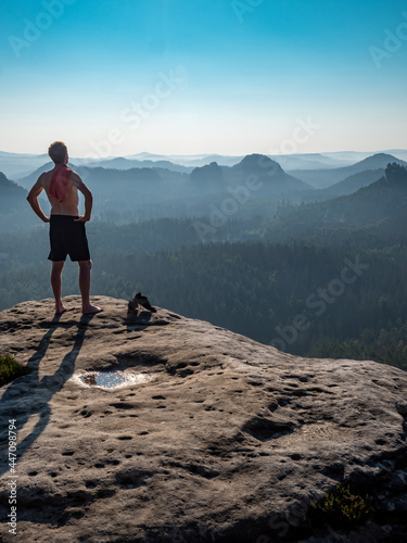 Naked man with a sporty figure on the edge of a rock enjoys the view of the morning landscape.
