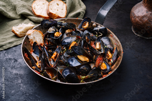 Traditional barbecue Italian blue mussel in tomato red wine sauce with baguette bread as close-up in a rustic iron pan