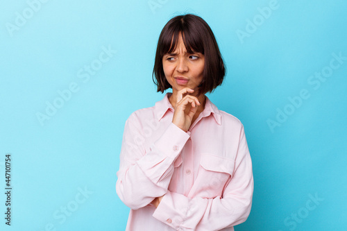 Young mixed race woman isolated on blue background looking sideways with doubtful and skeptical expression.