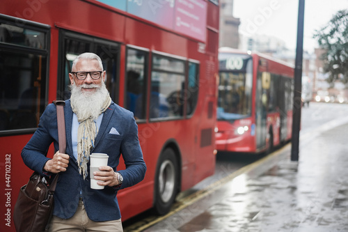 Senior business man going to work drinking coffee with london bus station in background - Focus on face