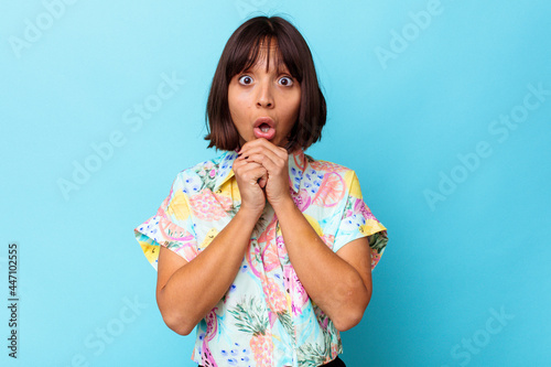 Young mixed race woman isolated on blue background praying for luck, amazed and opening mouth looking to front.
