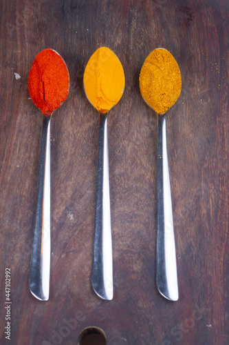 Indian Colourful Spices Also Know as Red Chilli Powder, Turmeric Powder, Coriander Powder, Mirchi, Mirch, Haldi, Dhaniya Powder Isolated on wooden Background in spoon.