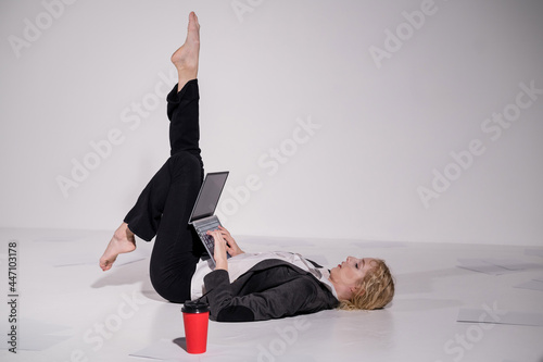 Barefoot ballerina dressed in a business suit poses for a laptop and drinks coffee. Flexible woman works at the computer