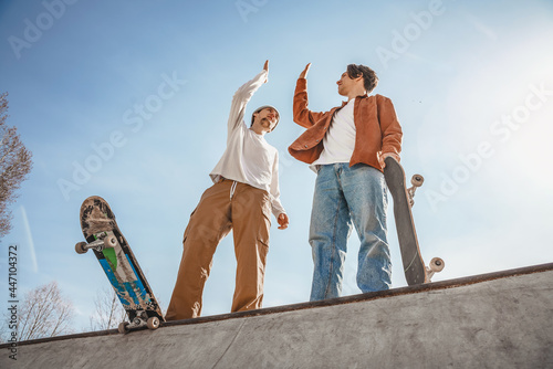 Two boys skaters stand on the highest ramp in a skatepark and encourage each other for a great workout, holding skateboards in their hands