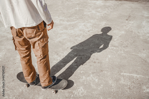 Skater calmly rides a skateboard, approaches the ramp in a gray skatepark, the sun reflects the shadow of the athlete