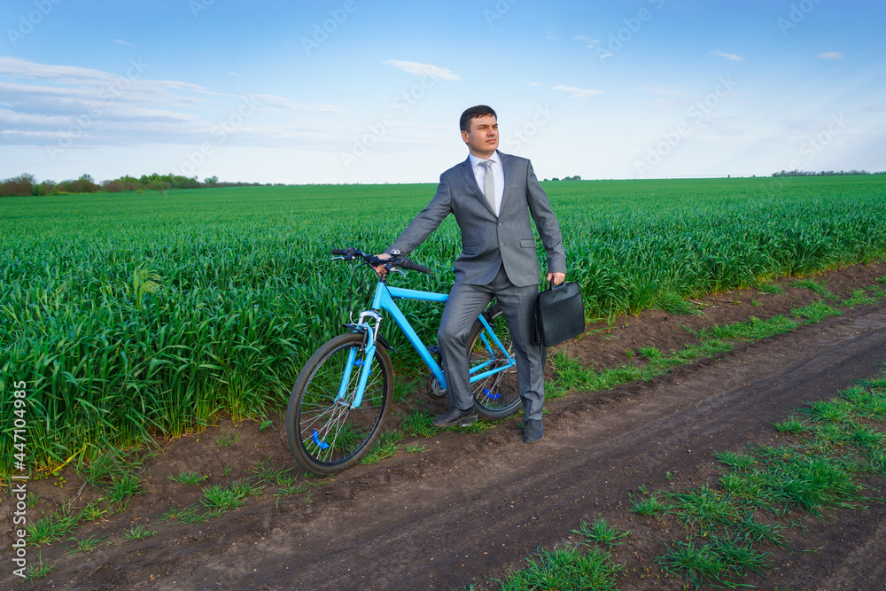 Obraz premium Businessman with a bicycle posing in a green grass field - business concept for freedom, vacation or freelance. Beautiful spring nature.