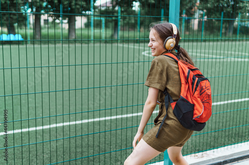 Teen schoolgirl on the way to the school. She is listening to music on headphones and holding a book. Education and back to school concept