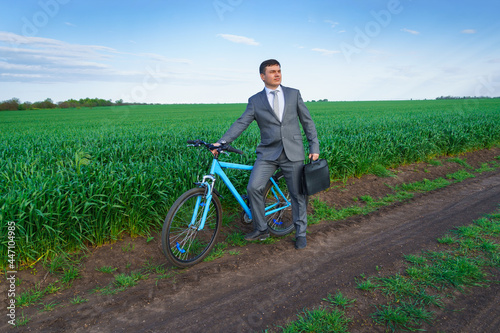 Businessman with a bicycle posing in a green grass field - business concept for freedom, vacation or freelance. Beautiful spring nature.