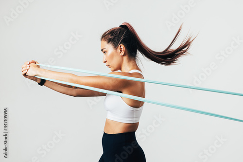 Side view of sportswoman exercising with resistance band against white wall