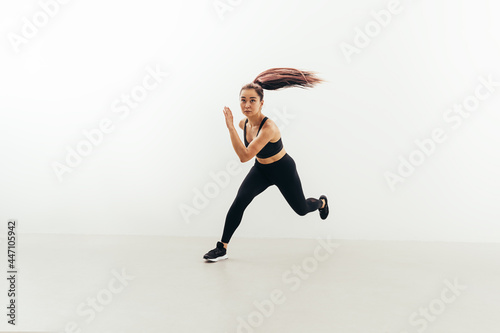 Front view of muscular woman running in studio against white wall