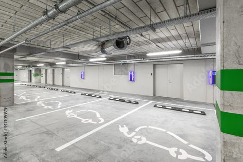 Empty public underground parking lot or garage interior with concrete stripe painted columns and signs. Electric car charging place.