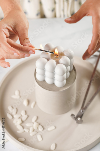 Female hands lighting a grey bubble candle on several concrete trays with a match