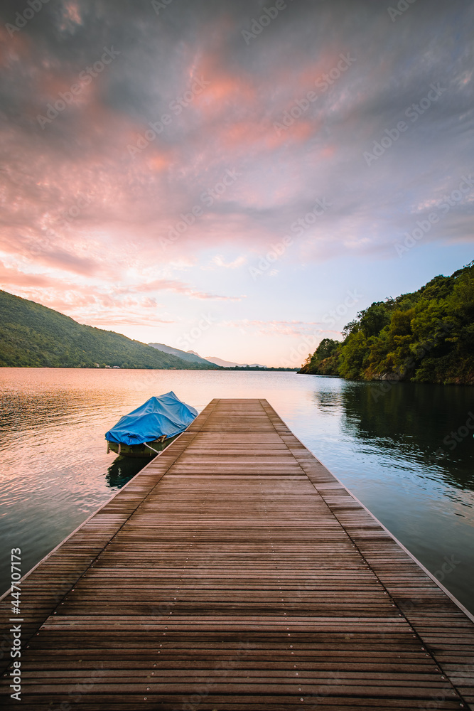 Obraz premium Mergozzo, Verbania / Italy - June 2021: Lake Mergozzo at dawn with wooden jetty in the foreground and colored clouds. Without people