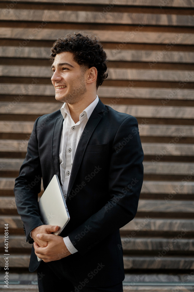 He holds a laptop with documents in his hands. A young entrepreneur in a business suit goes to work. A new business center in the city center. He holds a laptop with documents in his hands. A young entrepreneur in a business suit goes to work. A new business center in the city center.