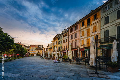 Orta San Giulio / Italy - June 2021: Main square of the village of Orta San Giulio at sunset with blue clouds, with people sitting in the bars / restaurants of the square