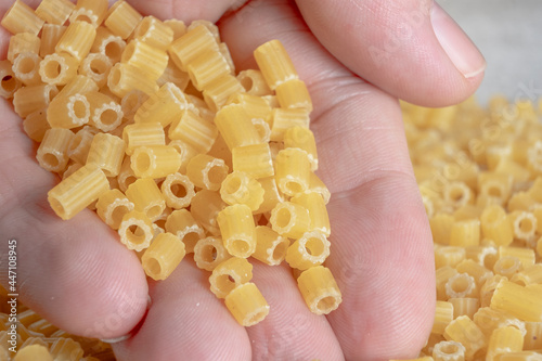 A male hand holding a pile of short ribbed tubes pasta. Mediterranean cuisine.