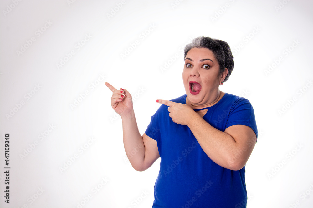 People diversity young lady with gray hair pointing with forefingers to the side with open mouth wearing blue on white background People diversity young lady with gray hair pointing with forefingers to the side with open mouth wearing blue on white background
