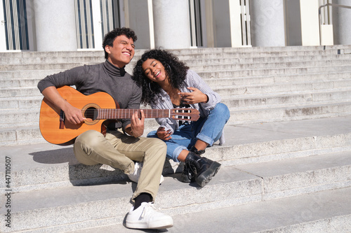 A young latin couple in love playing the guitar and singing sitting on stairs. Millennial generation.
