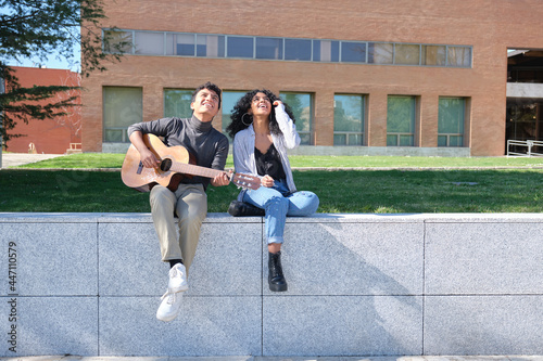 Young latin couple looking up to the sky and playing the guitar at the university campus. University life  millennial generation.