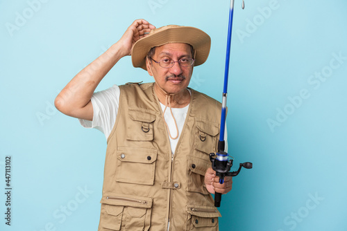 Senior indian fisherman holding rod isolated on blue background being shocked, she has remembered important meeting.
