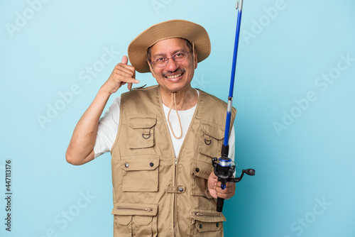 Senior indian fisherman holding rod isolated on blue background showing a mobile phone call gesture with fingers.