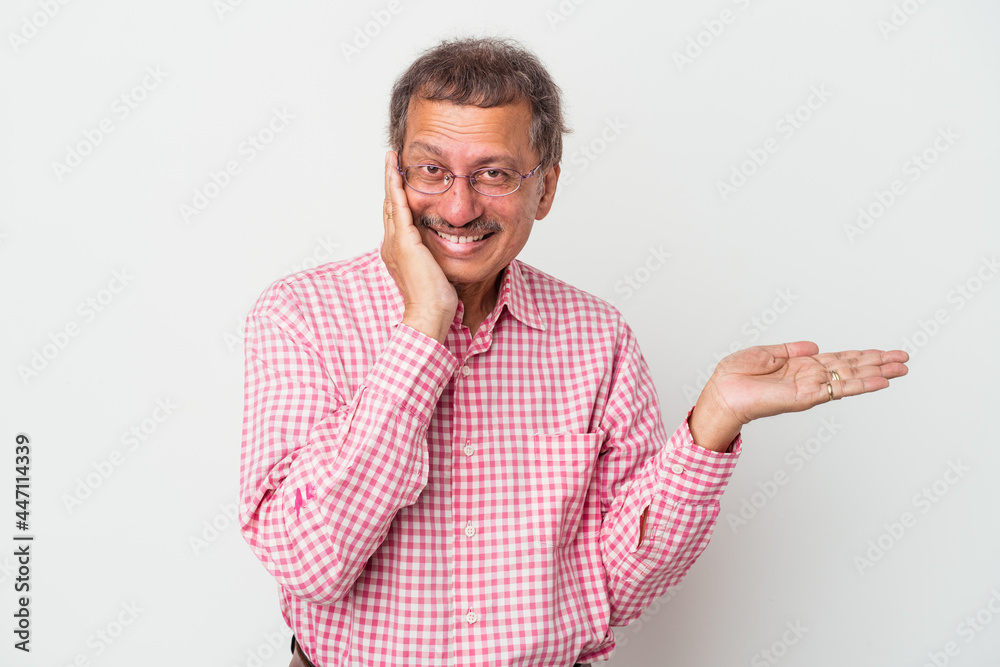 Middle aged indian man isolated on white background holds copy space on a palm, keep hand over cheek. Amazed and delighted. Middle aged indian man isolated on white background holds copy space on a palm, keep hand over cheek. Amazed and delighted.