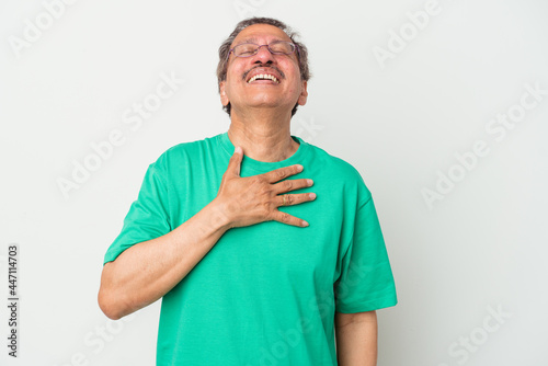 Middle aged indian man isolated on white background laughs out loudly keeping hand on chest. © Asier
