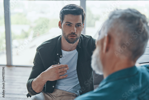 Schilderij op canvas Handsome young man talking to his senior father while spending time at home toge