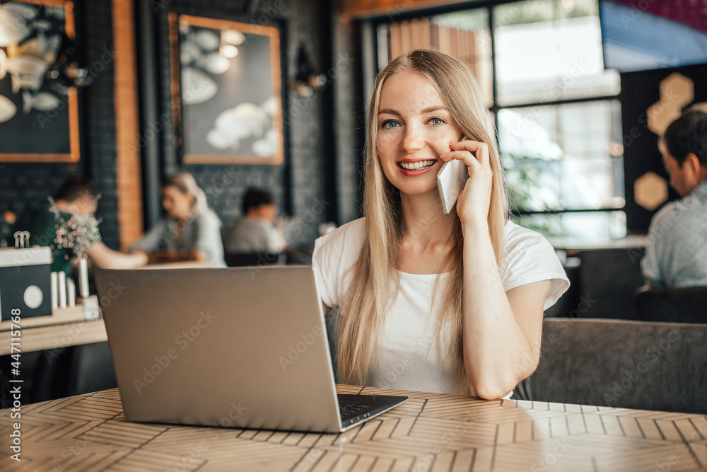 Young caucasian blonde freelancer woman in cafe with phone and laptop Young caucasian blonde freelancer woman in cafe with phone and laptop