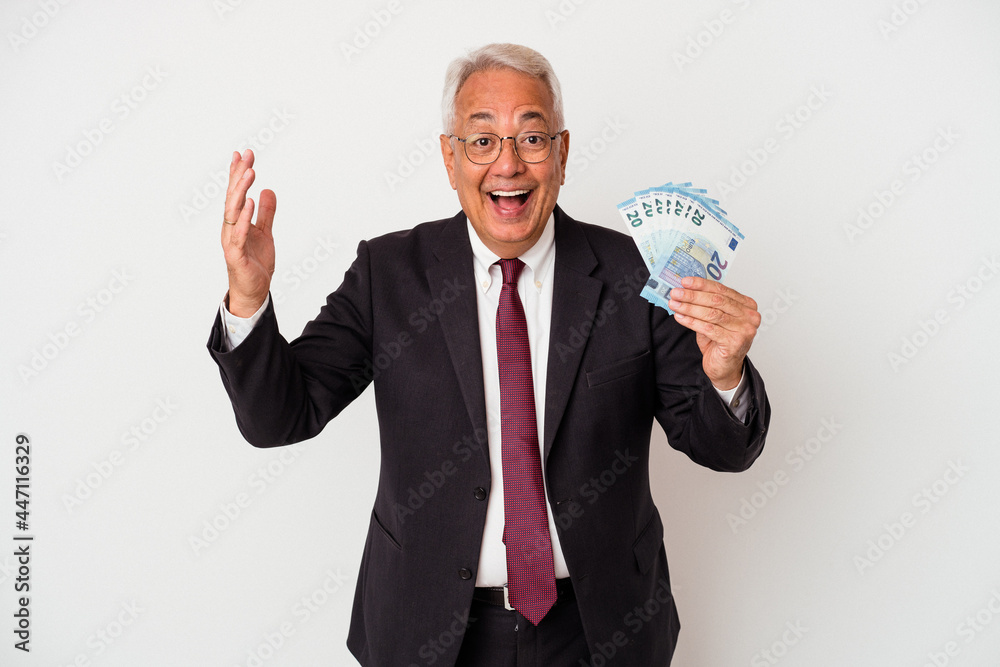 Senior american business man holding bills isolated on white background receiving a pleasant surprise, excited and raising hands. Senior american business man holding bills isolated on white background receiving a pleasant surprise, excited and raising hands.
