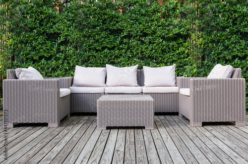 Leinwand Poster Beautiful wooden terrace with rattan garden furniture with greenery background