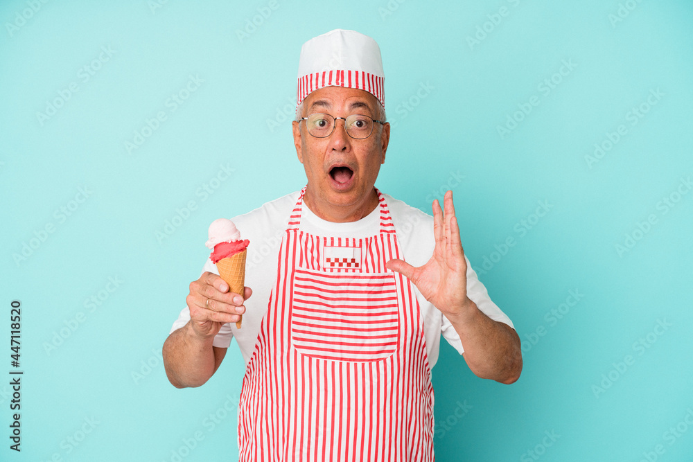 Senior american ice cream maker holding an ice cream isolated on blue background surprised and shocked. Senior american ice cream maker holding an ice cream isolated on blue background surprised and shocked.